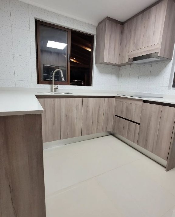 Cocina en L con muebles en madera clara, ventana con vistas al tejado y encimera blanca