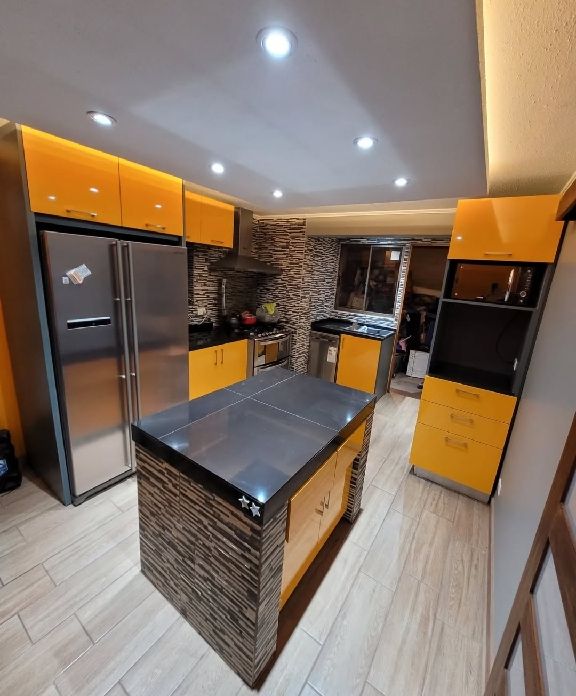 Cocina con muebles lacados en amarillo mostaza e isla central revestida en piedra oscura