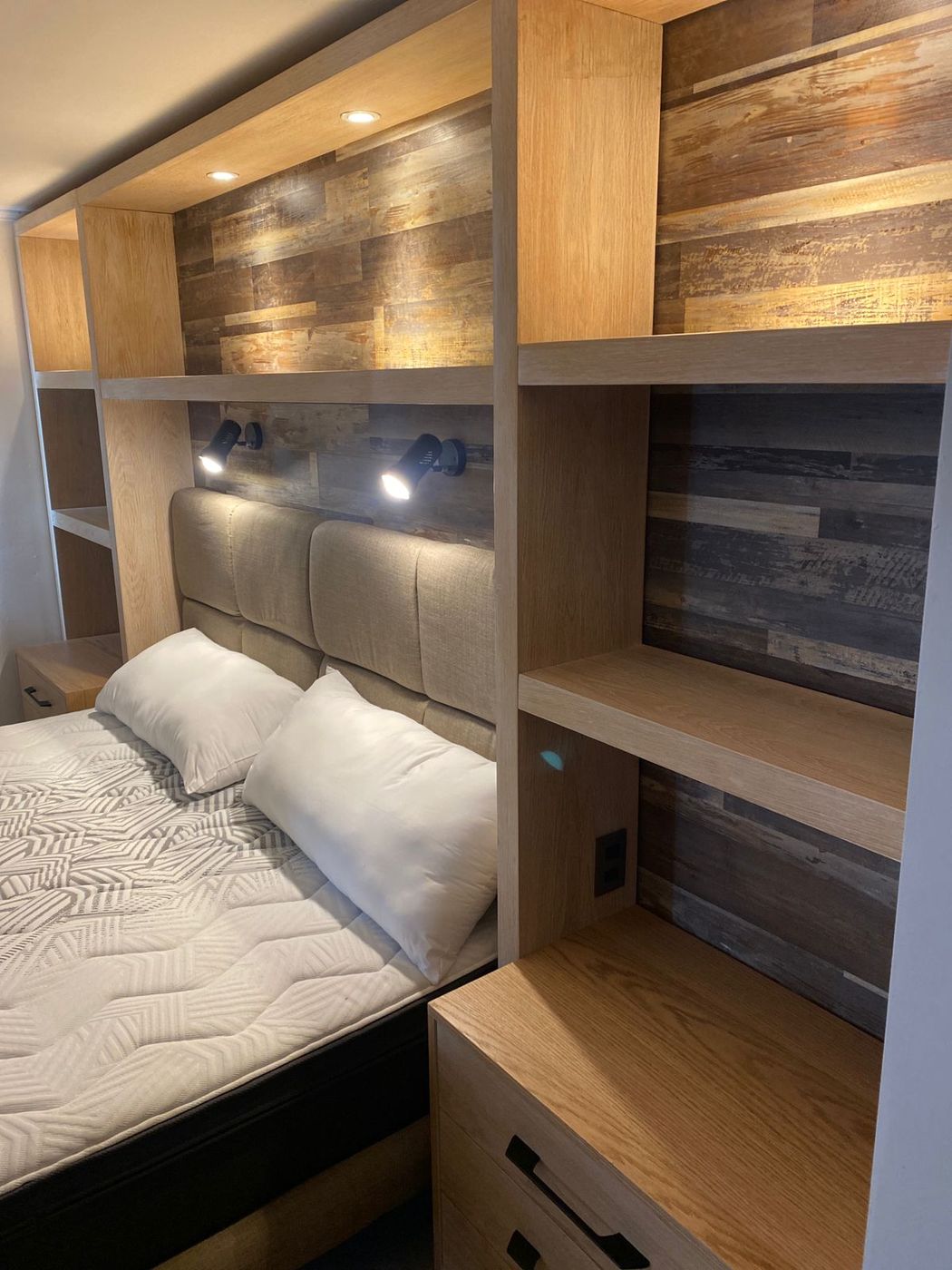 Detalle de cabecero tapizado con focos de lectura y panel de madera envejecida