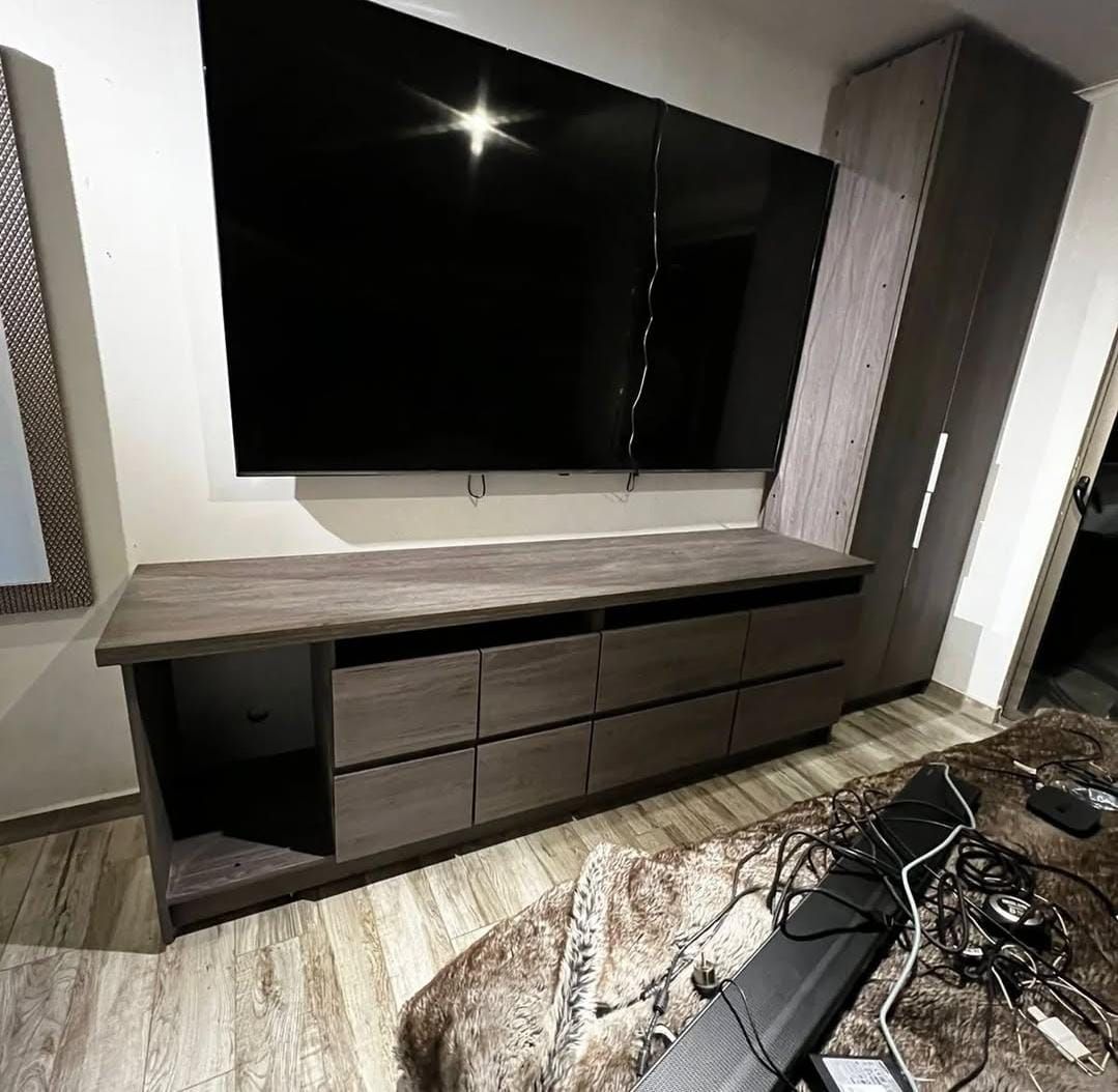 Detalle de mueble de televisión con cajoneras en madera grisácea y estante superior continuo