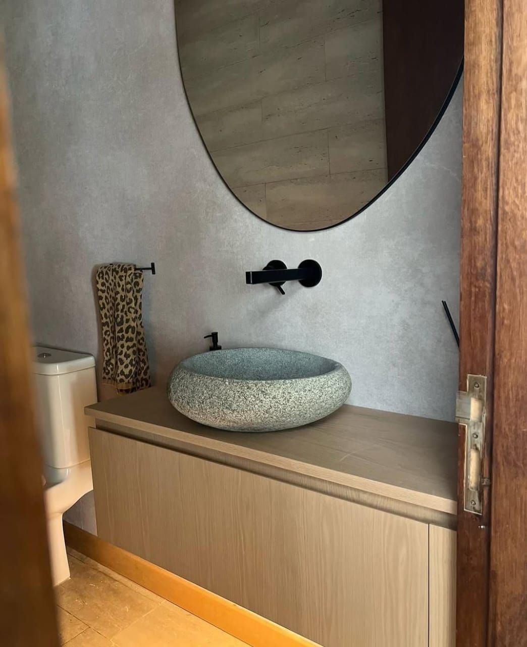 Aseo con lavabo de piedra gris sobre encimera de madera y grifería negra empotrada