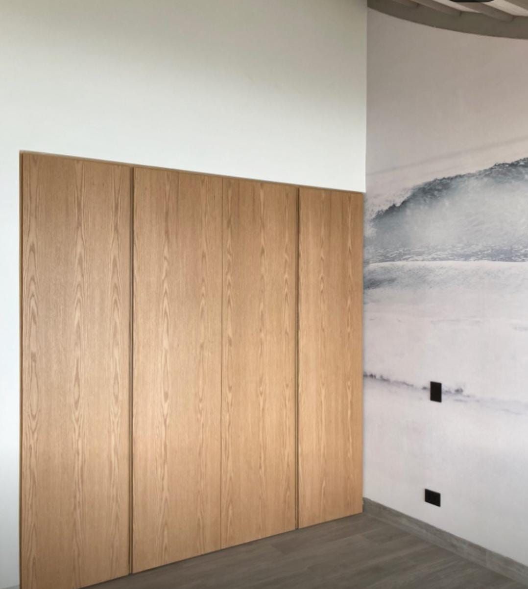 Puertas de armario empotrado en madera clara junto a pared con mural de olas