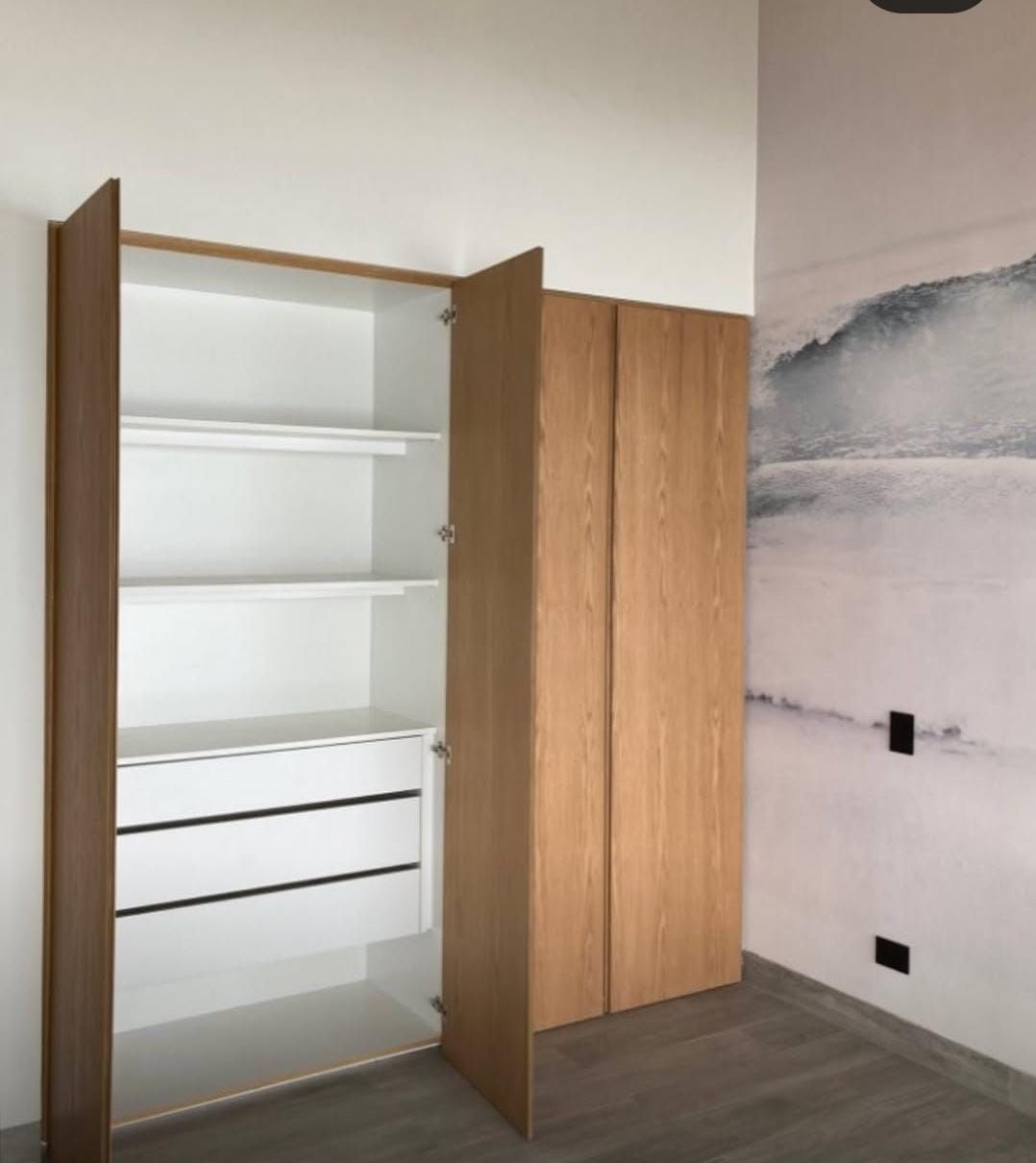 Armario de una puerta abierta con interior blanco, barra y cajones, junto a mural de olas