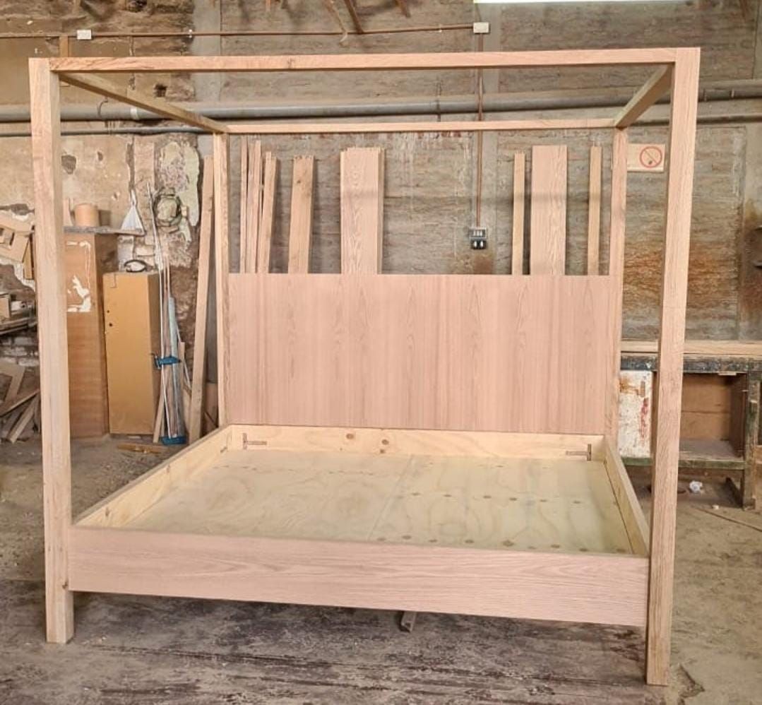 Estructura de cama con dosel en madera natural sin barnizar, en taller de carpintería