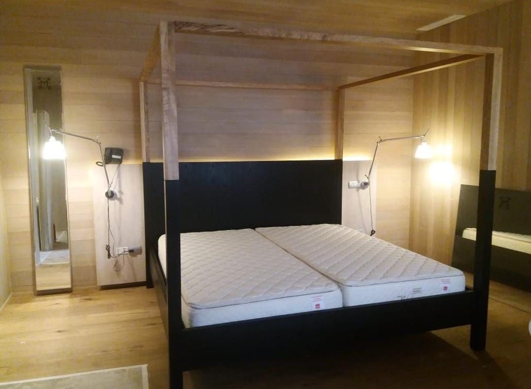 Cama con dosel de madera y cabecero negro, revestimiento de pared en madera clara