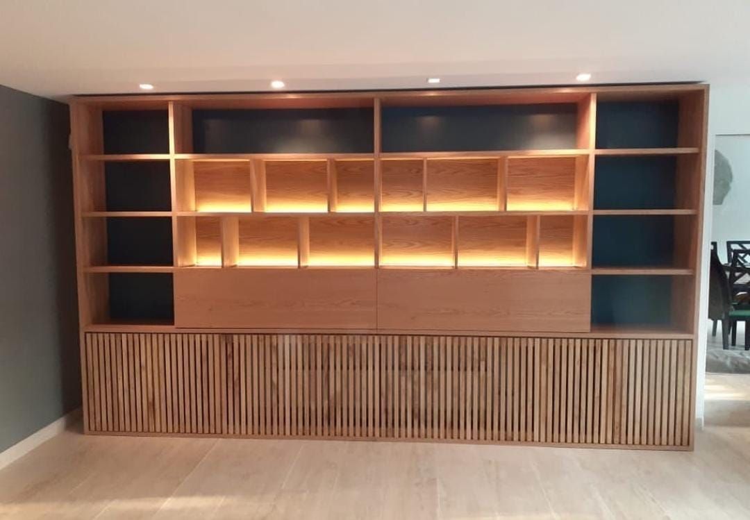 Librería en madera clara con cubículos iluminados y cajones de lamas verticales