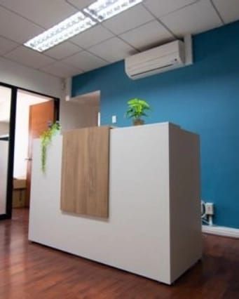 Mostrador de recepción blanco con frente de madera y pared azul petróleo