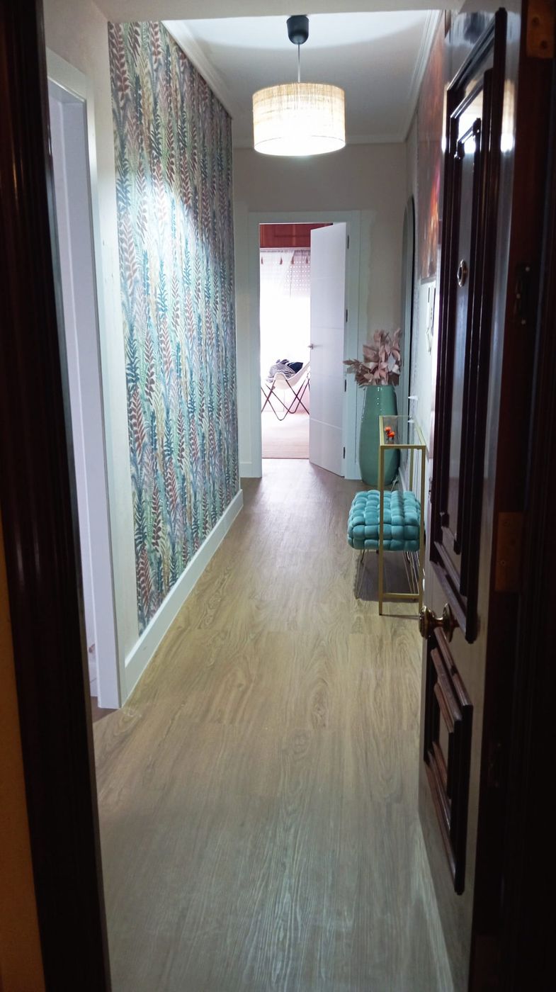 Pasillo de entrada en una vivienda de Ferrol, con papel pintado de hojas y banco tapizado