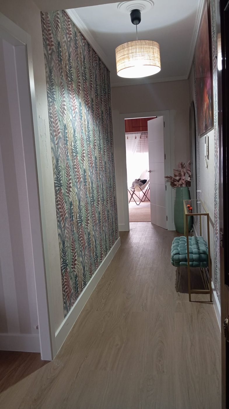 Vista de pasillo con papel pintado botánico, banqueta capitoné turquesa y jarrón decorativo