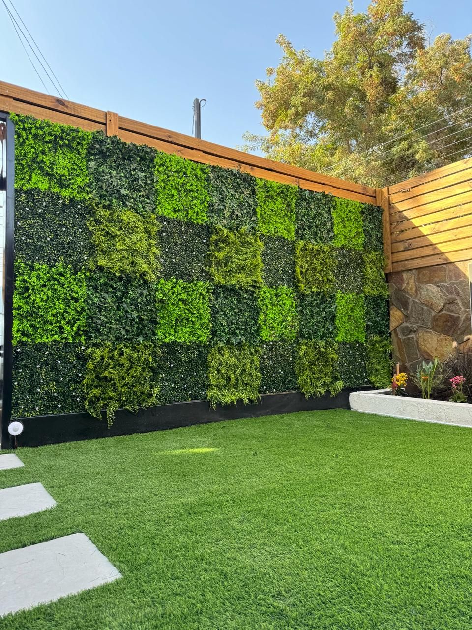 Jardín vertical artificial en mosaico de verdes sobre valla de madera y césped artificial