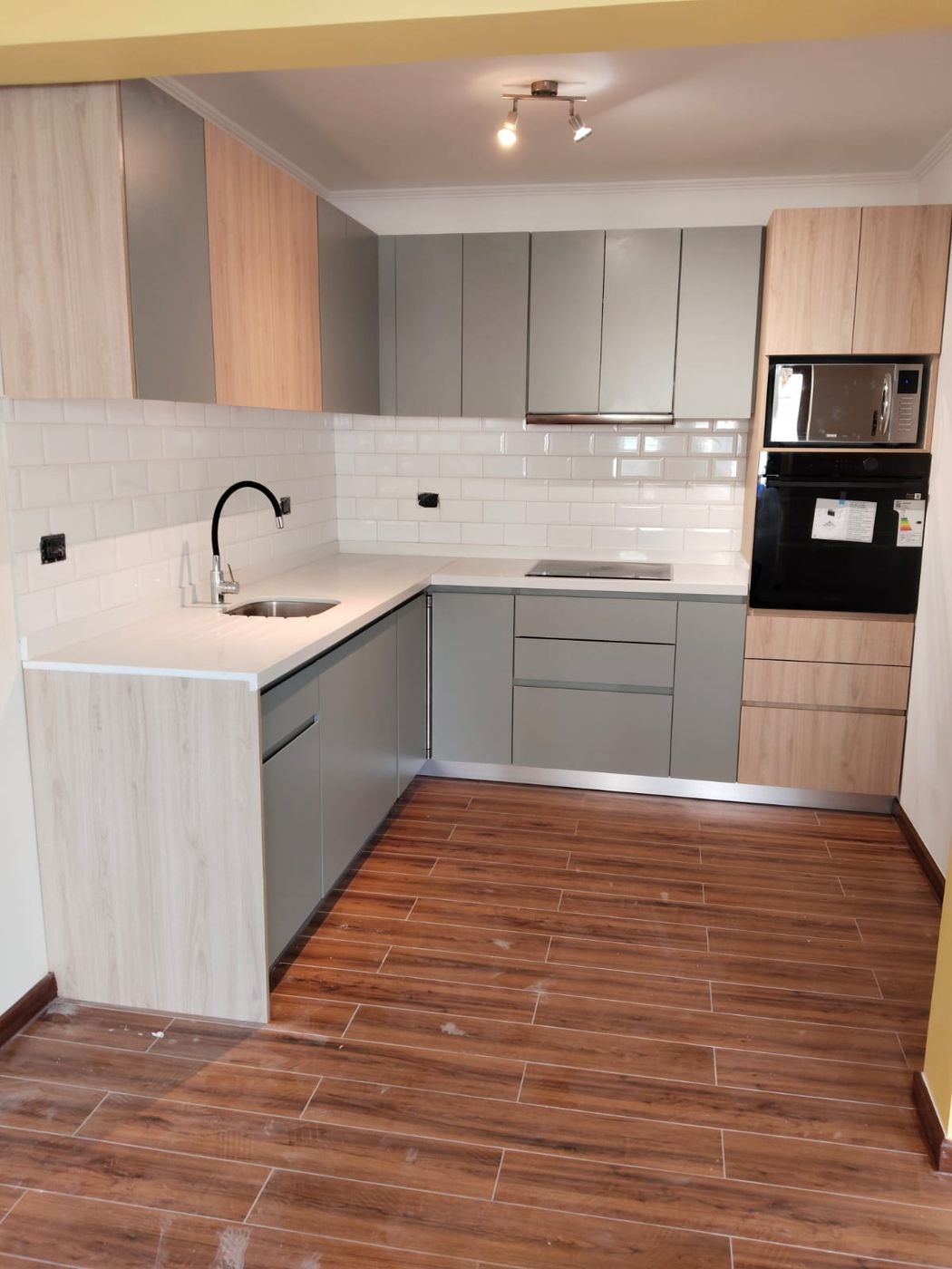 Cocina en L a dos tonos, gris y madera clara, con alicatado blanco tipo metro
