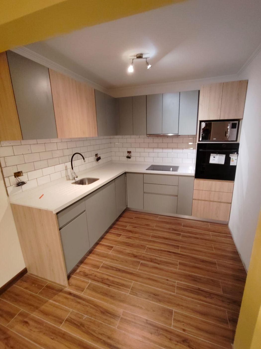 Vista amplia de cocina en L con fregadero, placa y columna de electrodomésticos