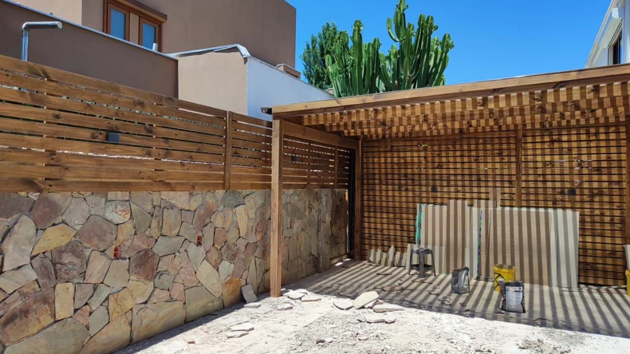 Pérgola de madera con muro de piedra natural y cerramiento de lamas junto a acceso