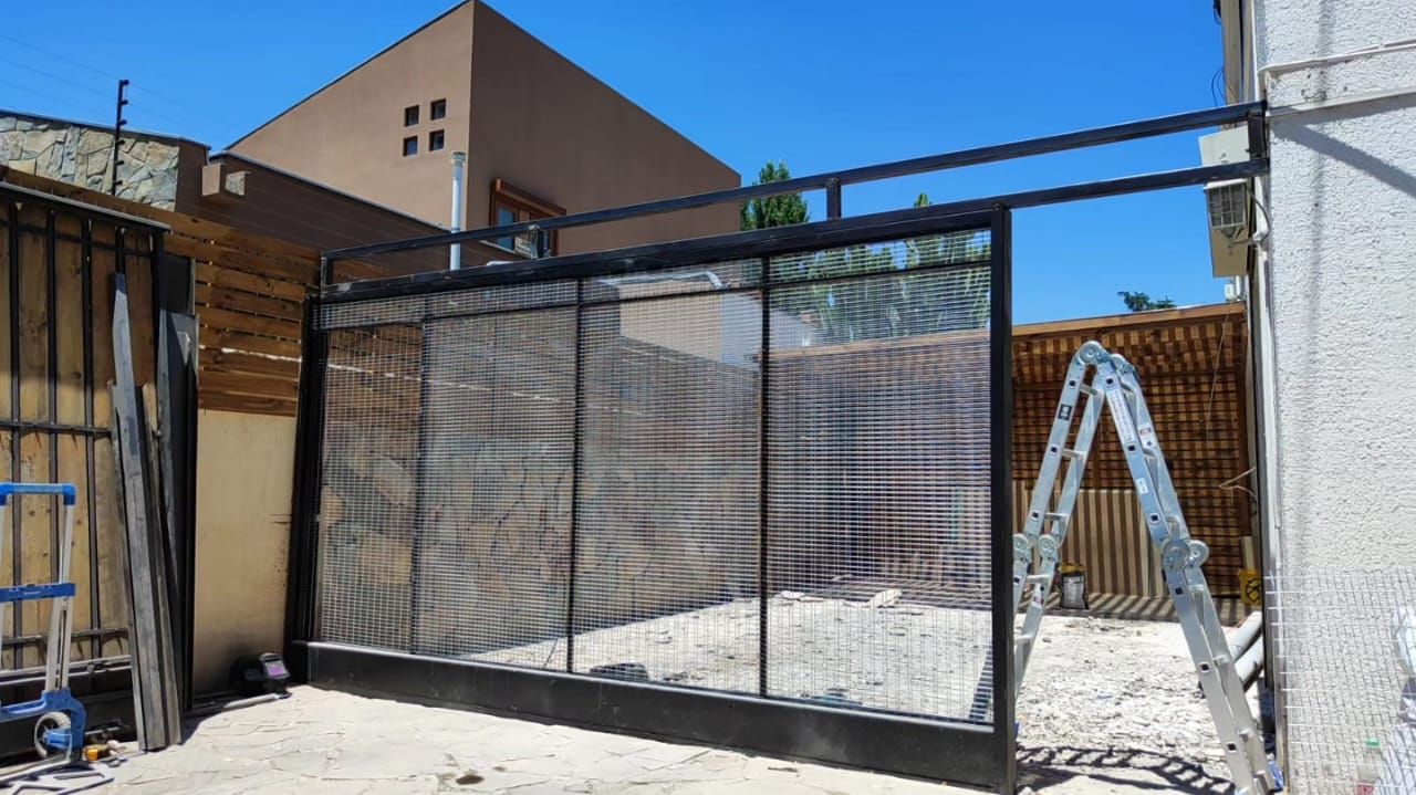 Cerramiento metálico con malla para terraza junto a valla de madera y muro de piedra