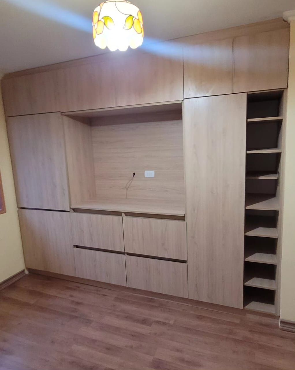 Mueble de dormitorio en madera clara con hueco central para televisor y zapatero lateral