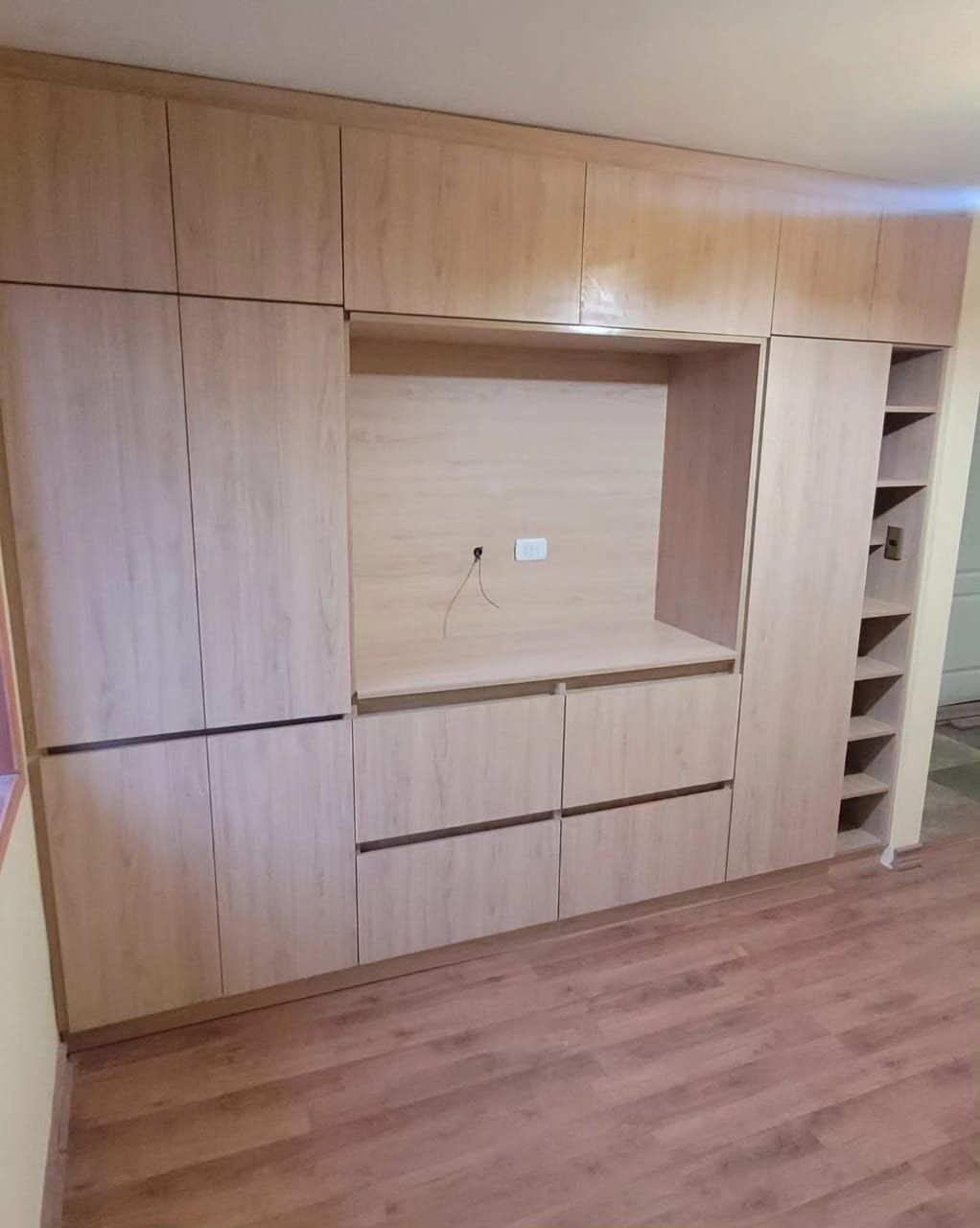 Panelado a medida en madera clara con hueco de televisor y armario zapatero de baldas
