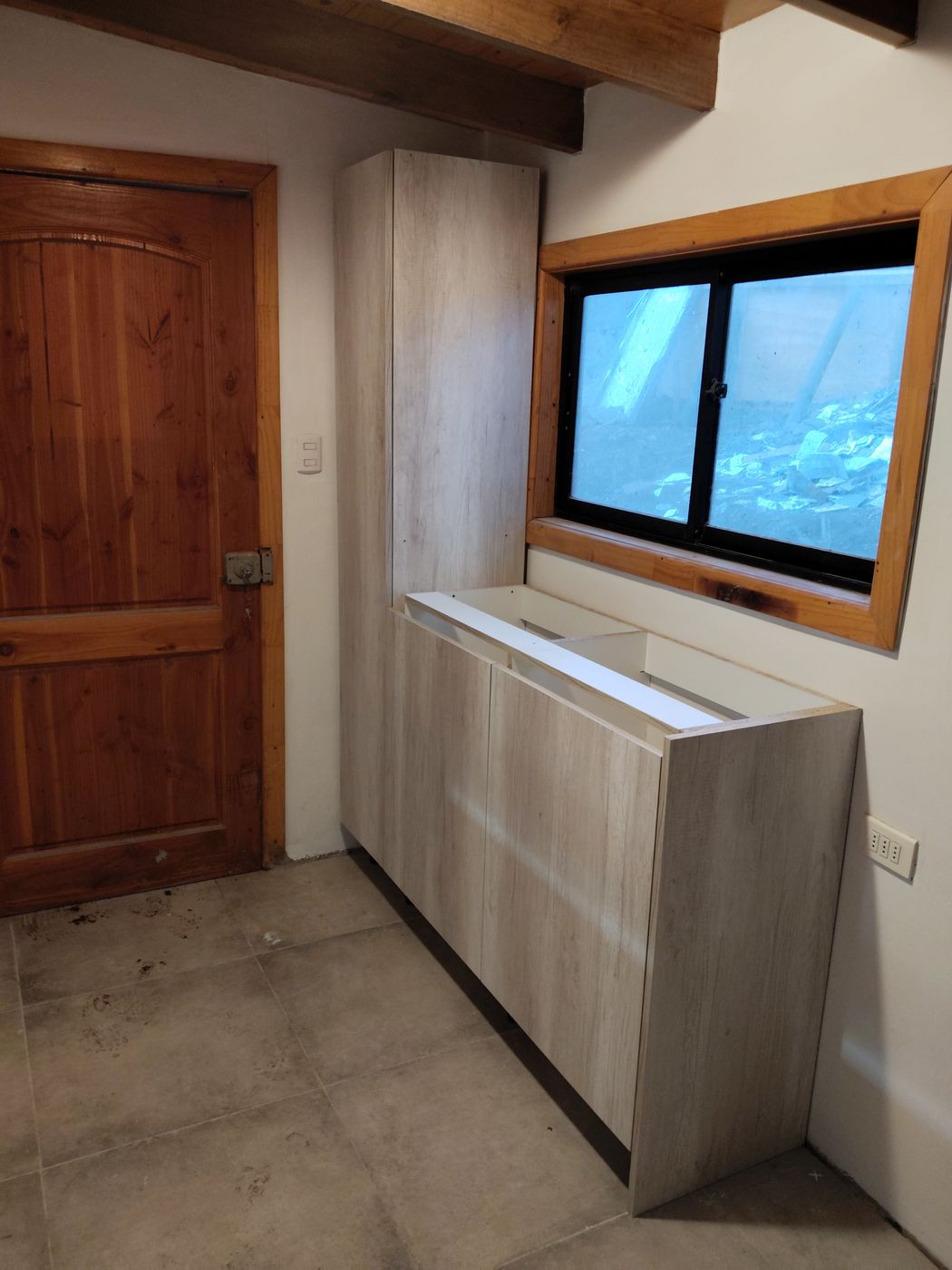Mueble bajo a medida en tonos grises claros junto a ventana de madera, en fase de instalación
